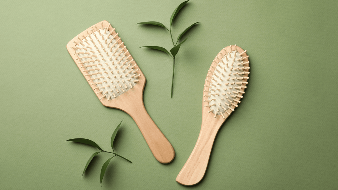 Bilden visar två hårborstar med träskaft och vita borst, placerade på en grön bakgrund. Runt borstarna ligger några gröna blad, vilket ger en naturlig och organisk känsla. Designen är enkel och elegant, framhävande hållbarhet och estetik.